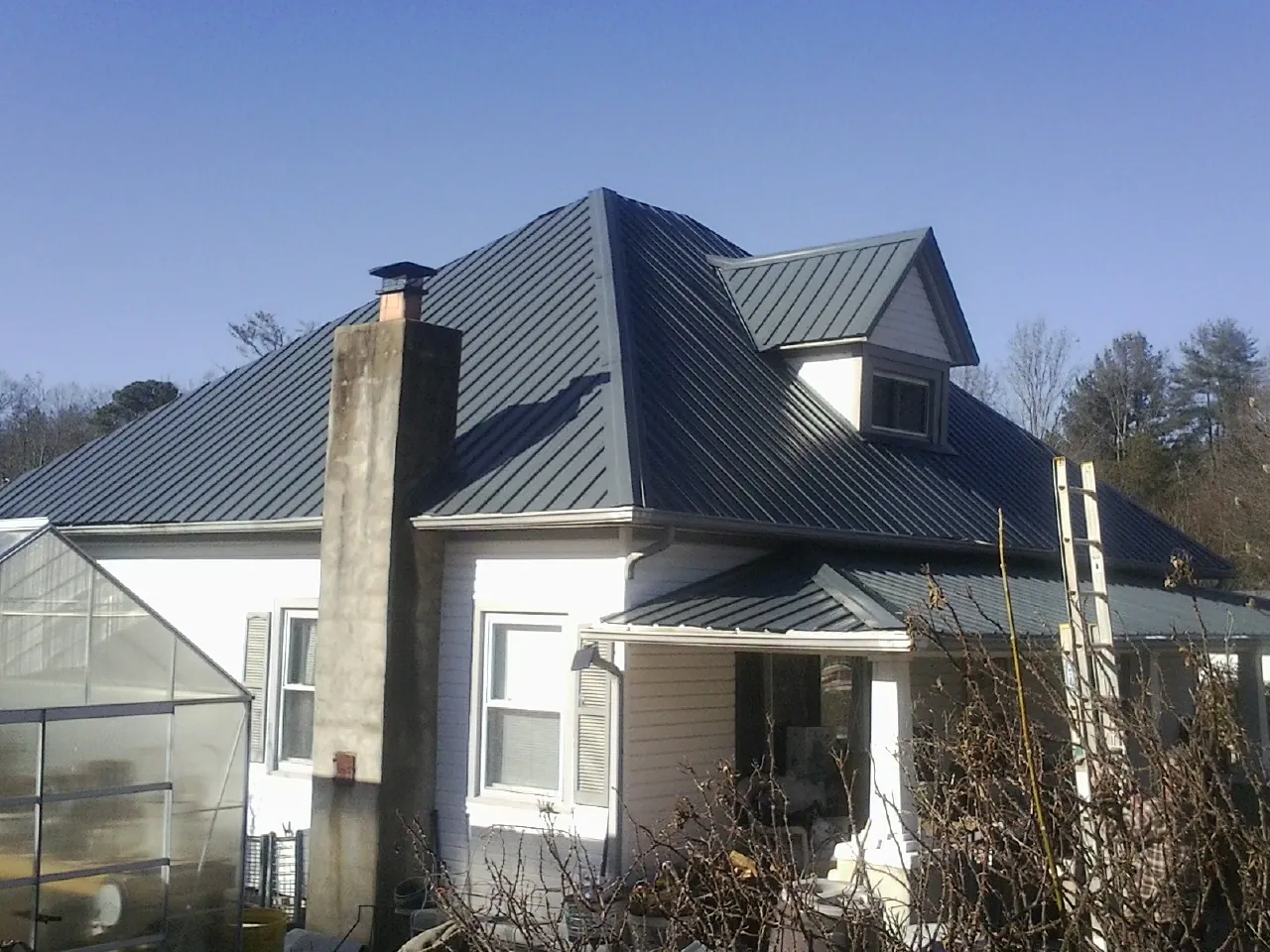 Dark blue standing seam metal roof on a white farmhouse with dormer — Slate & Tile Roof Repair by Roofing Brothers in Parker