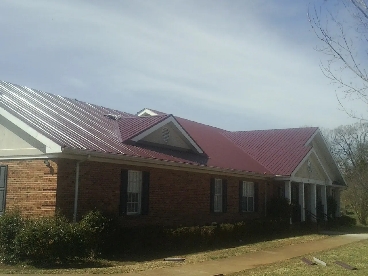 Red metal roof with gabled entries on a long brick building, from a Hail Damage Roof Repair job in Parker