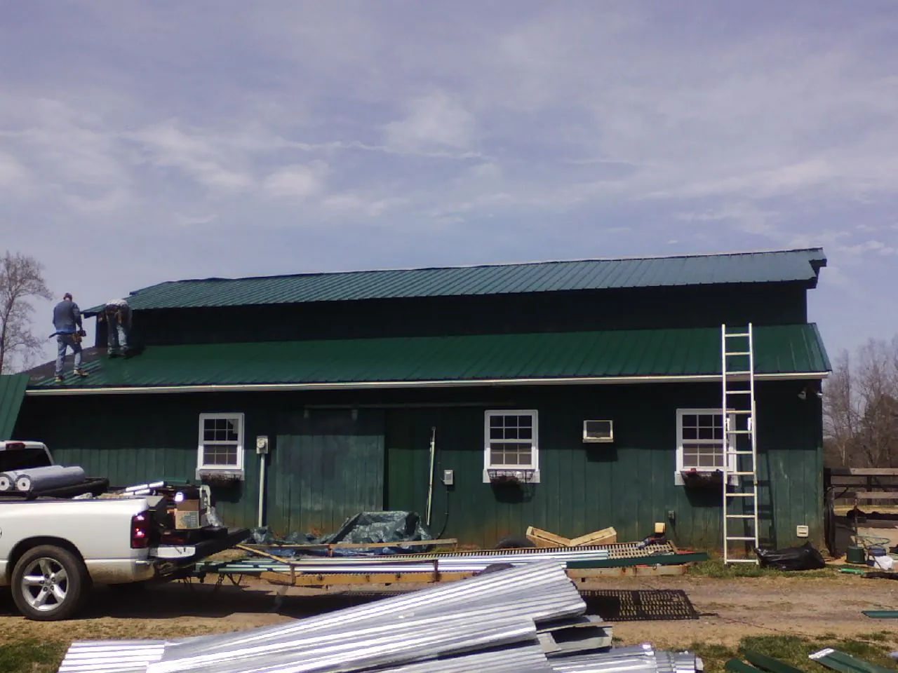 Crew installing green metal roofing on a large green barn in Parker